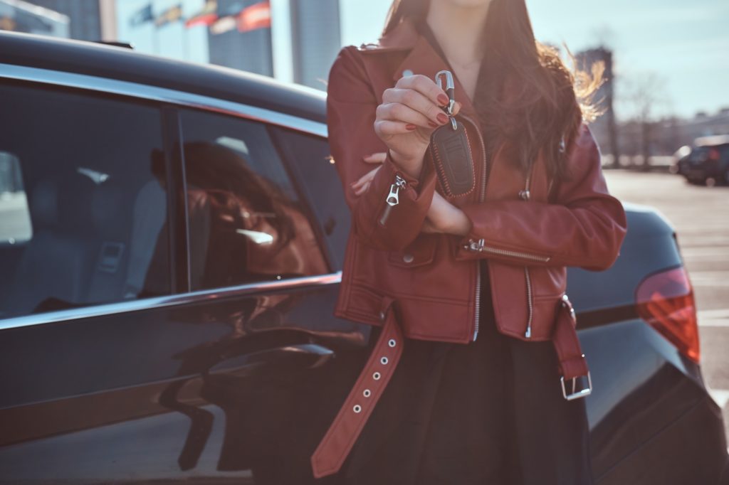 Women in red leather jacket just sold her car, which is behide her